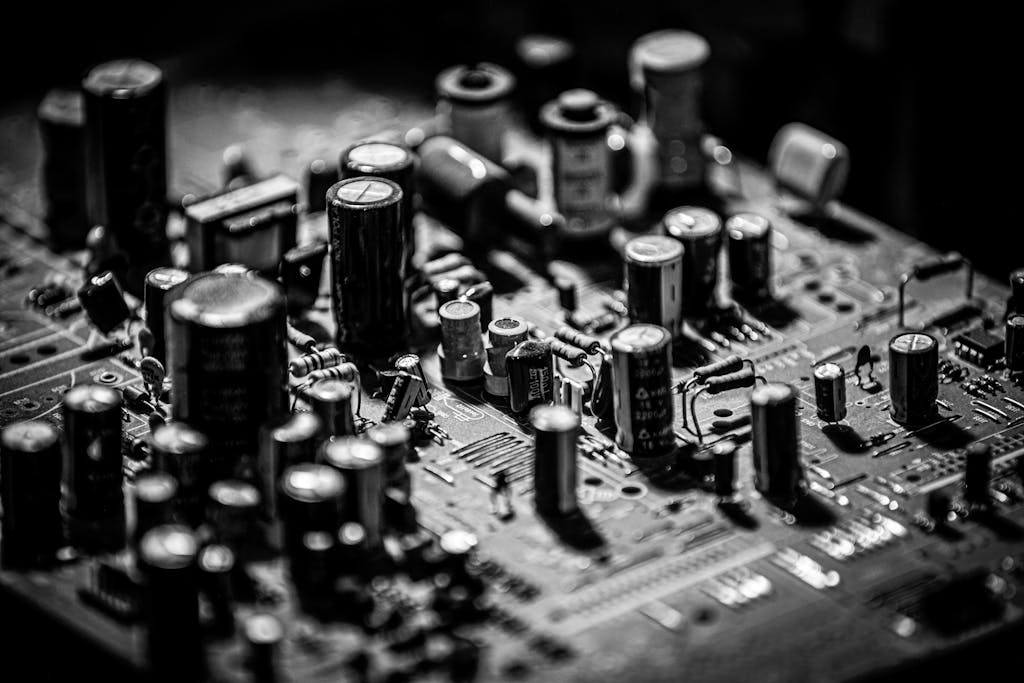 Grayscale close-up of electronic circuit board with capacitors and transistors.